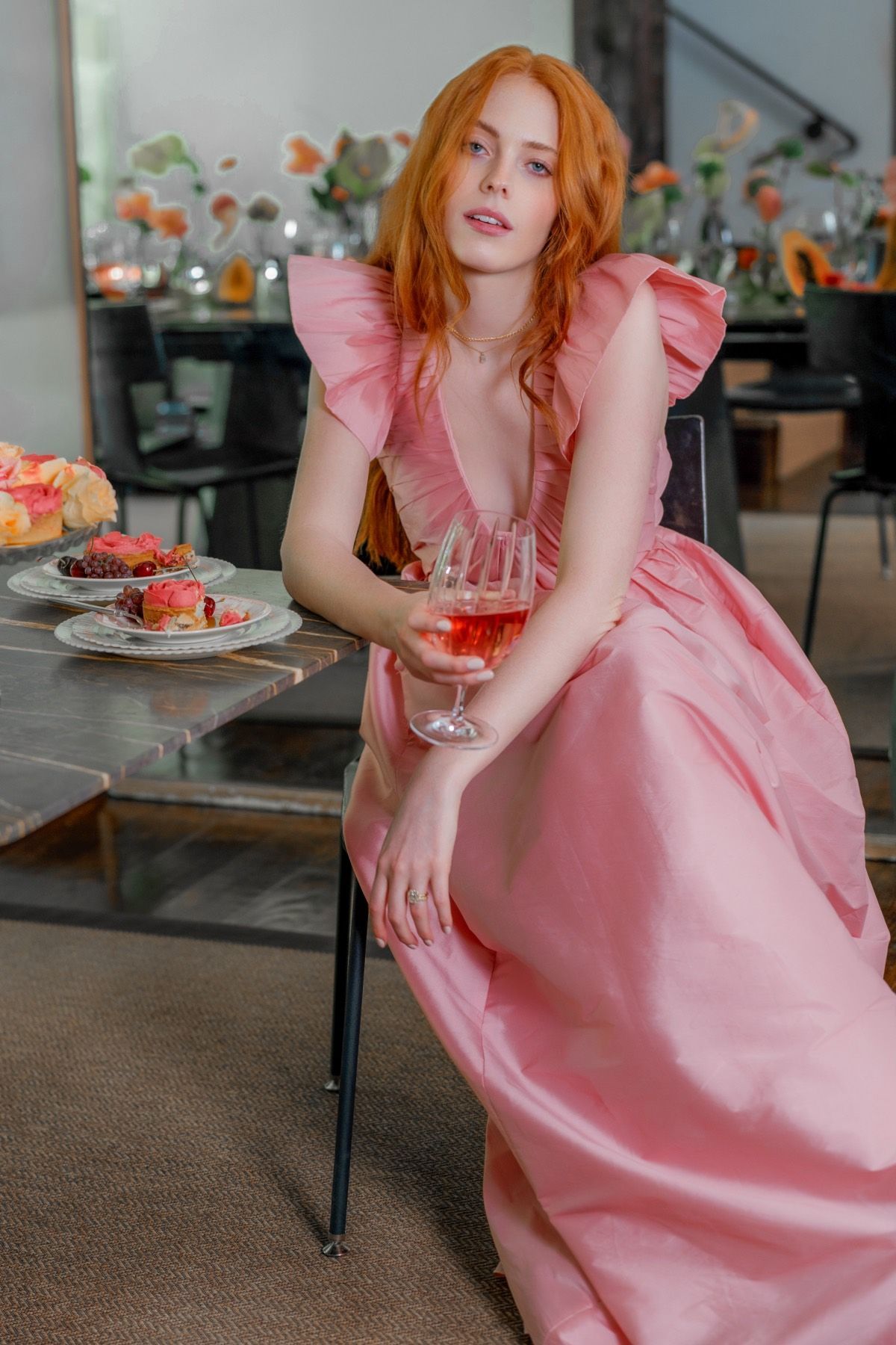 A woman in a pink dress is sitting on a chair holding a glass of wine.