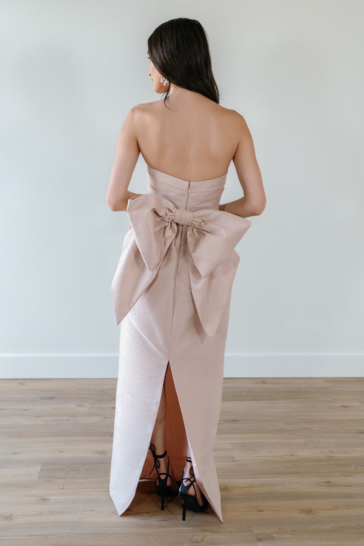 The back of a woman wearing a strapless dress with a bow on the back.