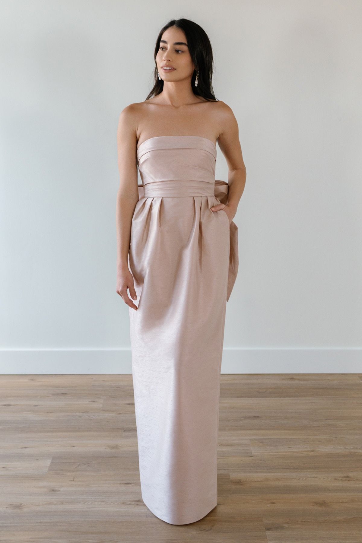 A woman in a strapless pink dress is standing on a wooden floor.