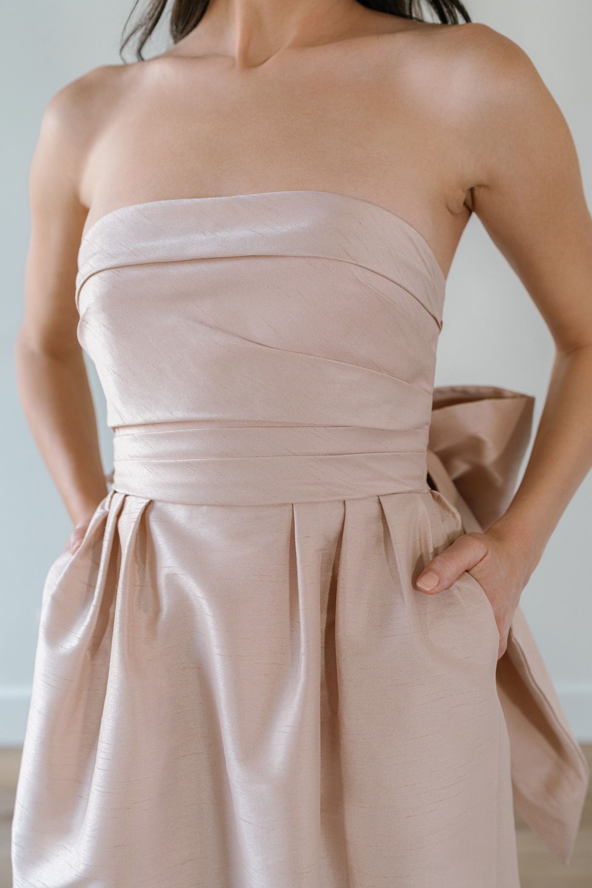 A woman is wearing a strapless dress with a bow on the waist.