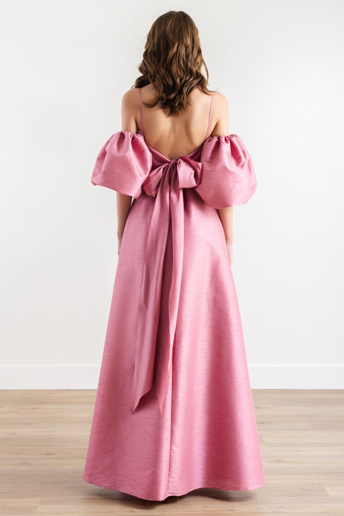 The back of a woman wearing a pink dress with a bow on the back.