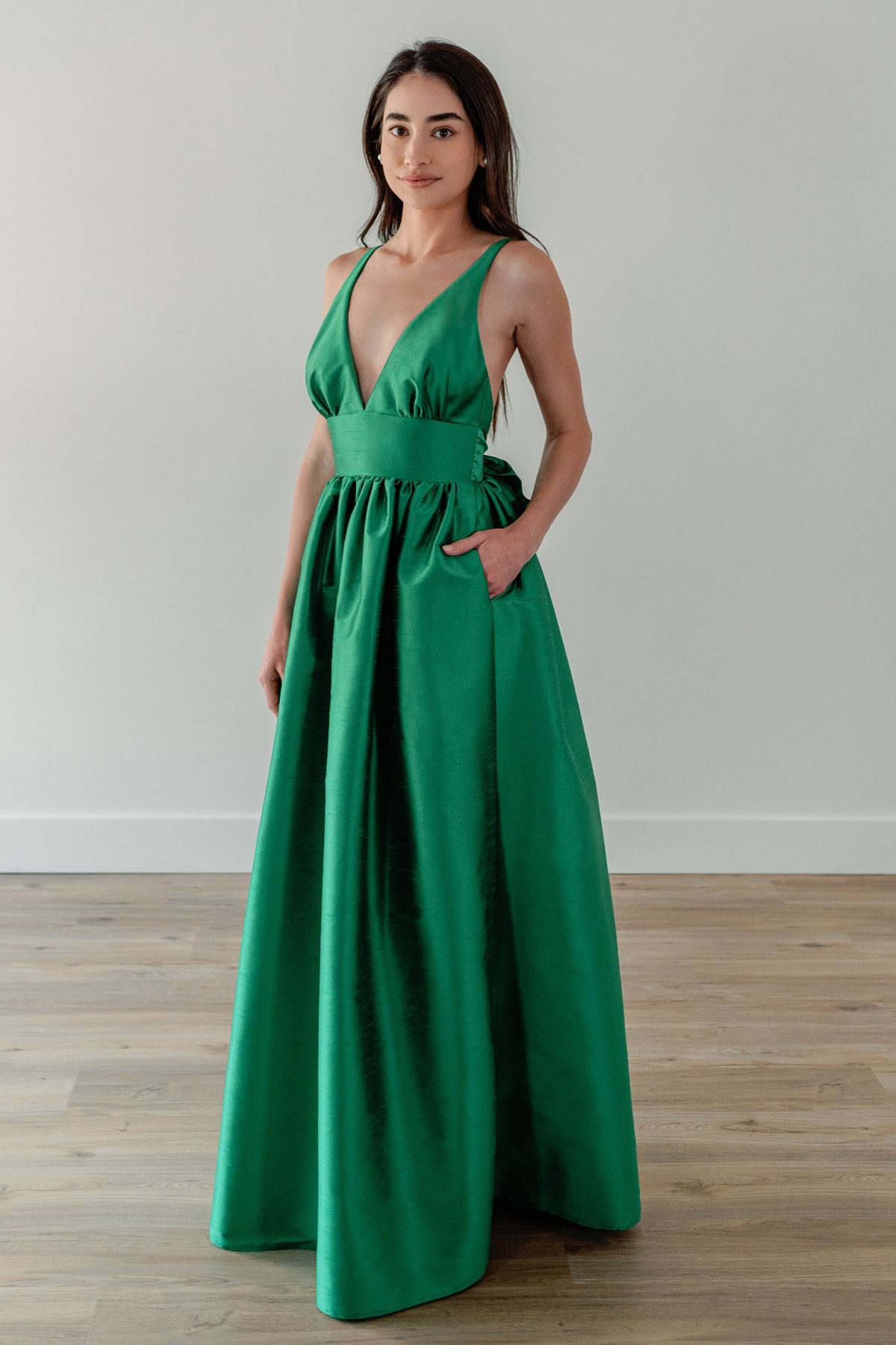 A woman is wearing a long green dress with pockets.