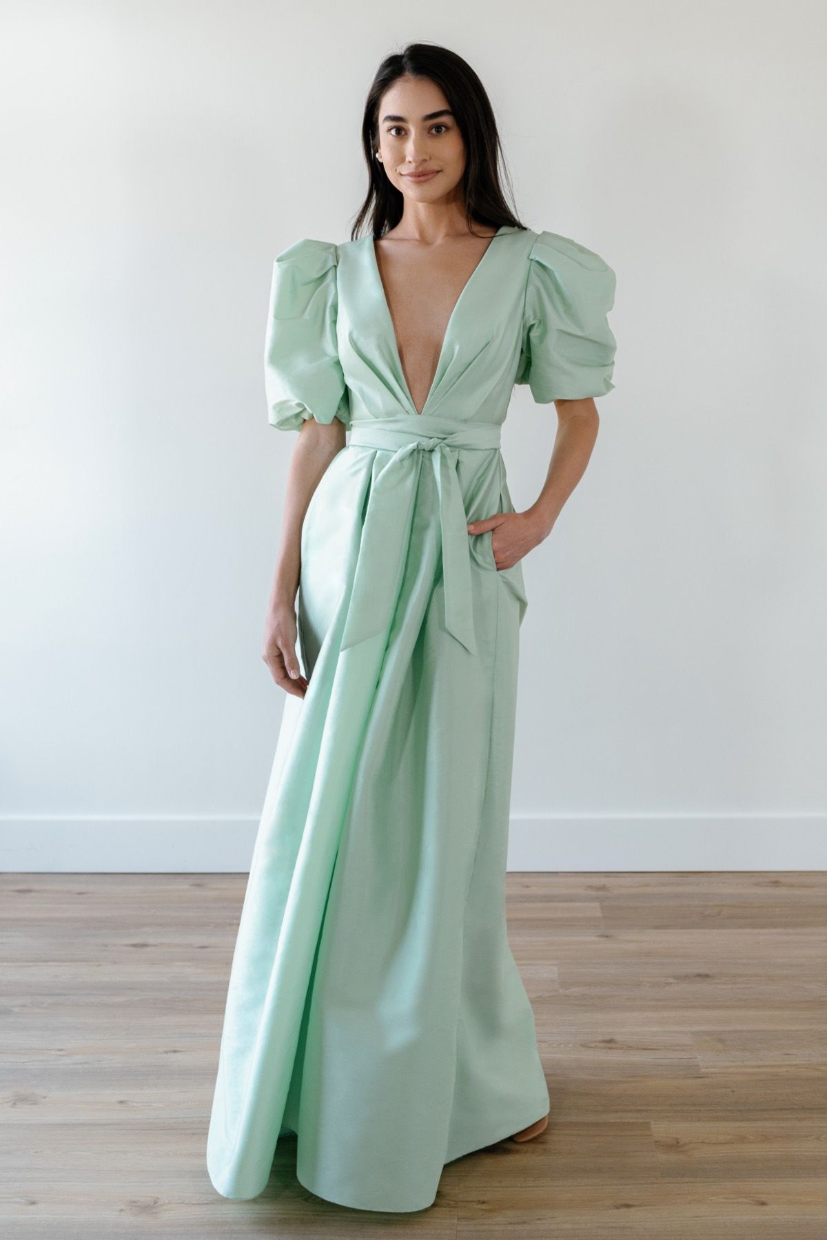 A woman is wearing a mint green dress with puffed sleeves and a plunging neckline.