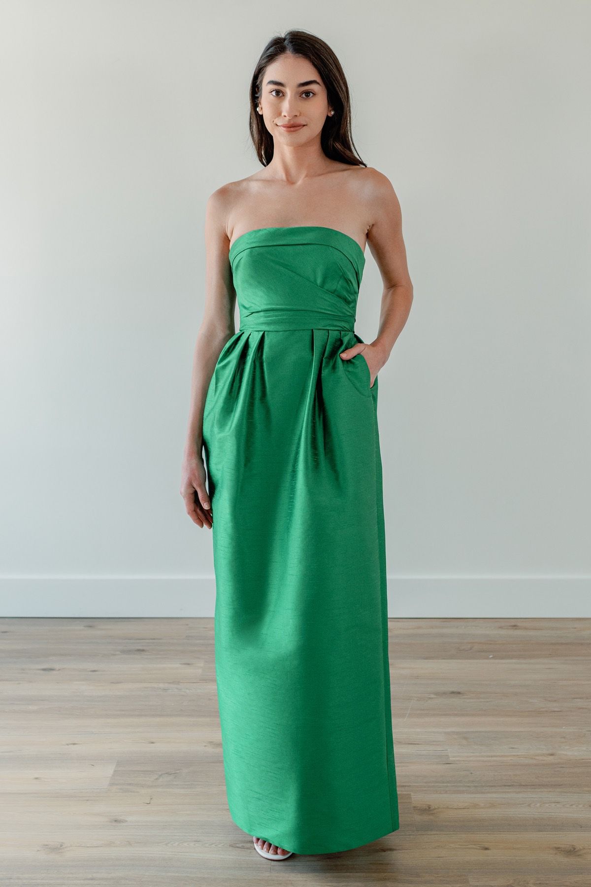 A woman is wearing a green strapless dress with pockets.