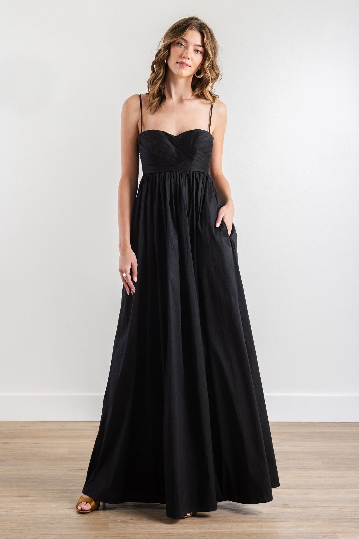 A woman is wearing a long black dress with pockets.