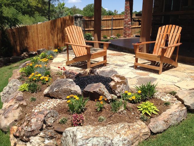 Two wooden chairs on a stone patio beside a landscaped rock garden and wooden fence