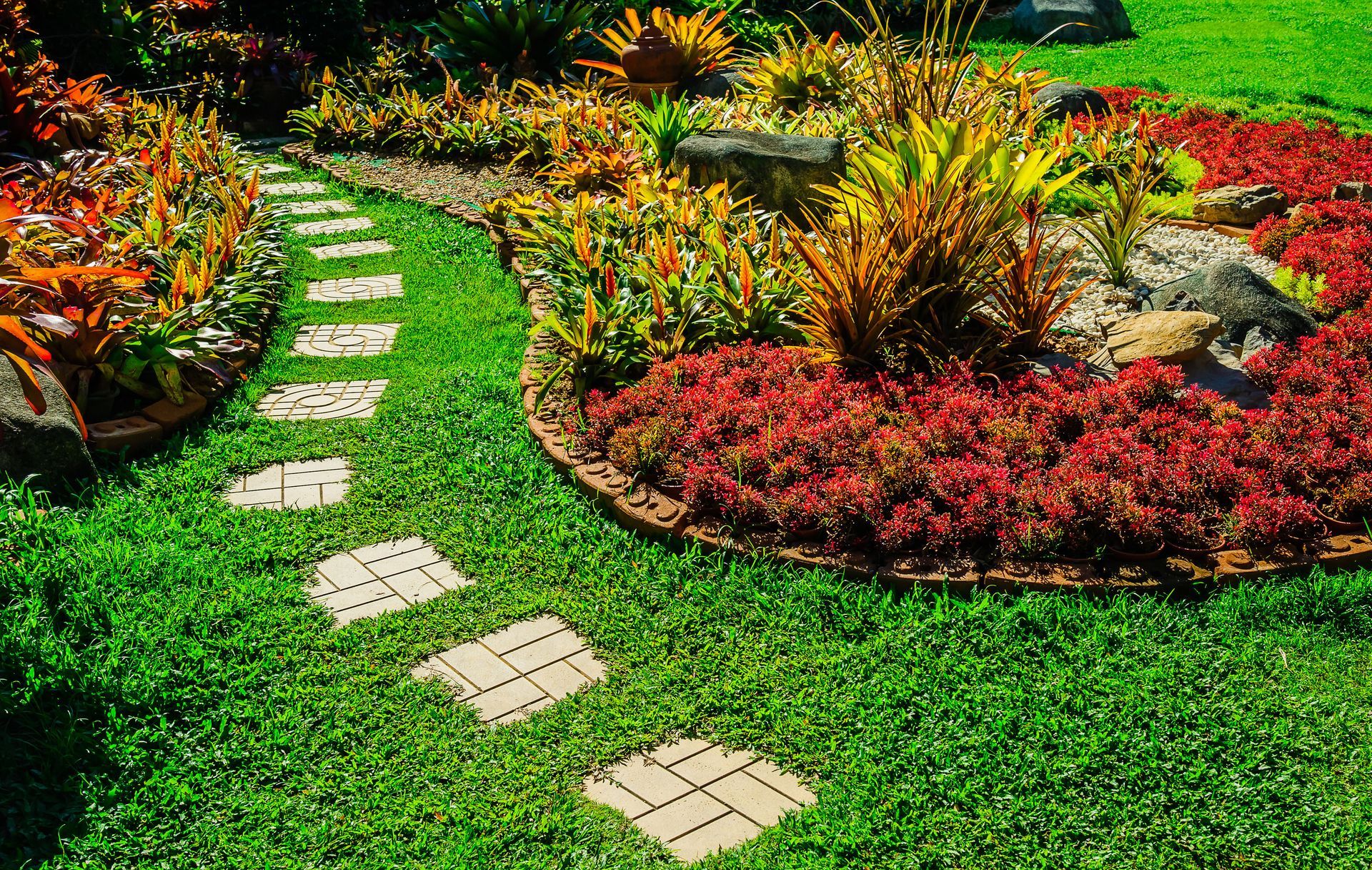 Curved stepping-stone path through a colorful flower garden with green grass and red-orange plants