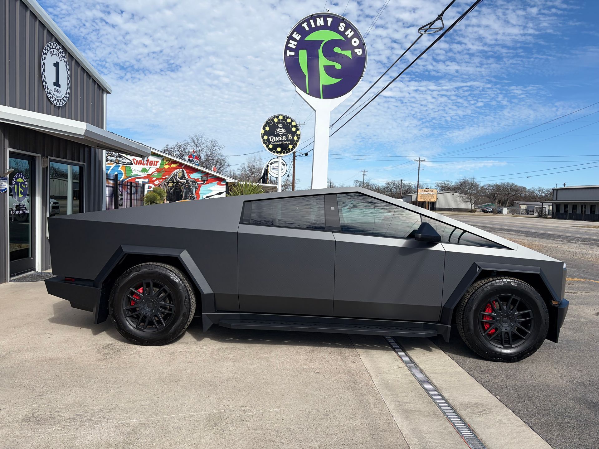 Gray Tesla Cybertruck parked outside The Tint Shop storefront with black wheels and red brake calipers.