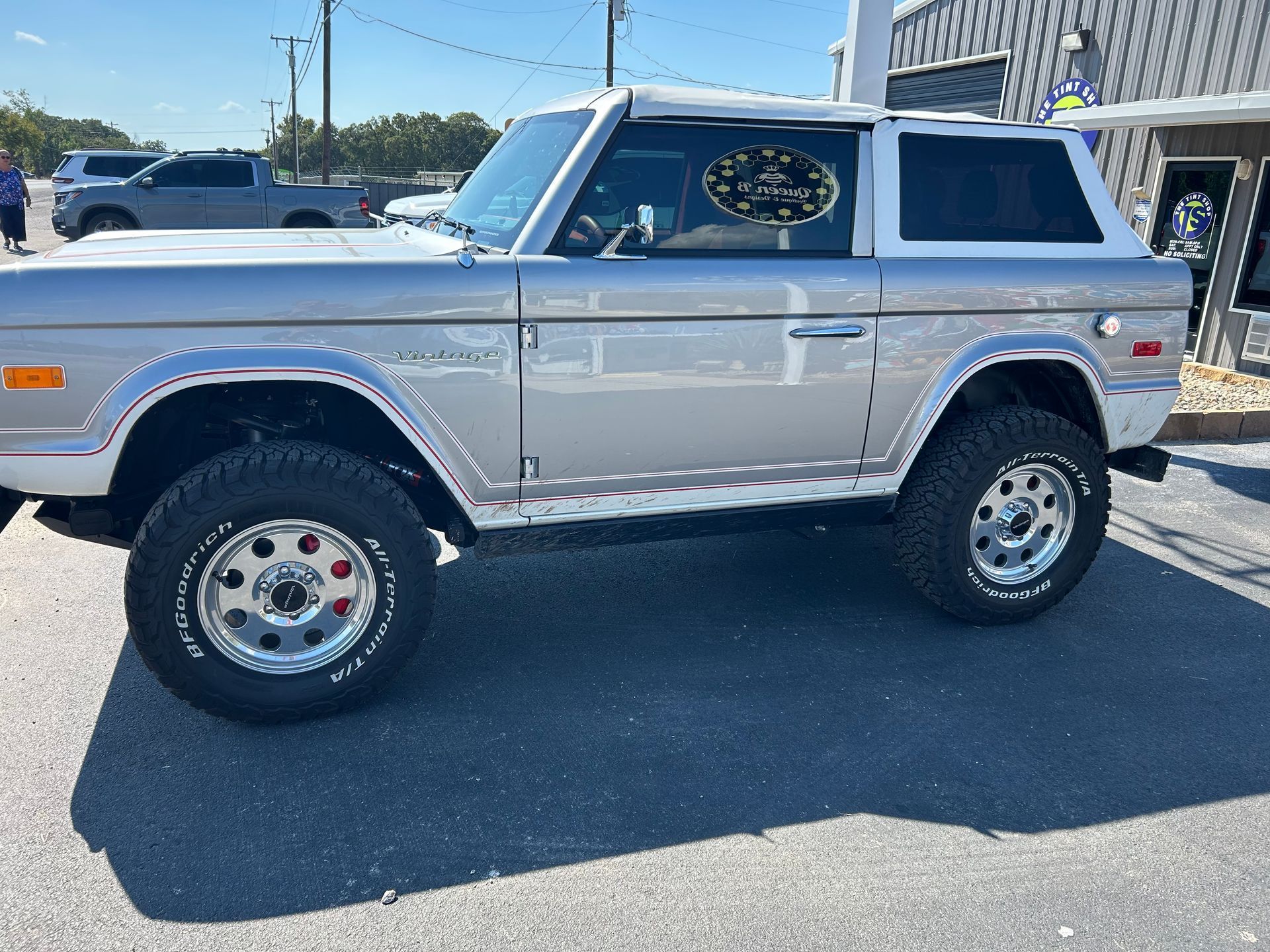 Silver and white vintage Ford Bronco parked on asphalt, sunny day.