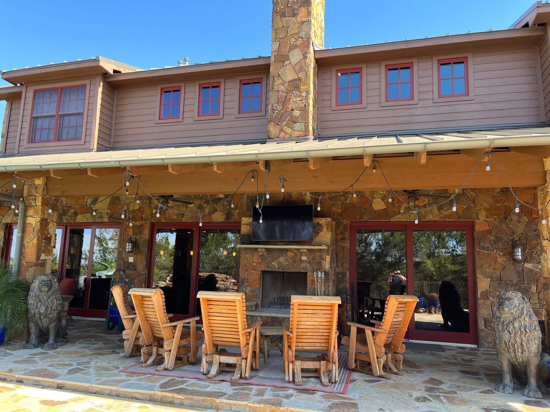 Two-story stone house with a patio, fireplace, and wooden rocking chairs. String lights hang above.