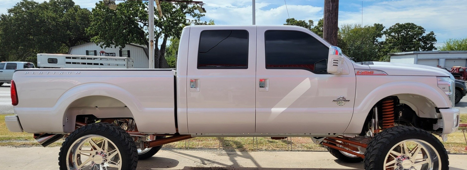 White lifted pickup truck with large chrome wheels and tinted windows.