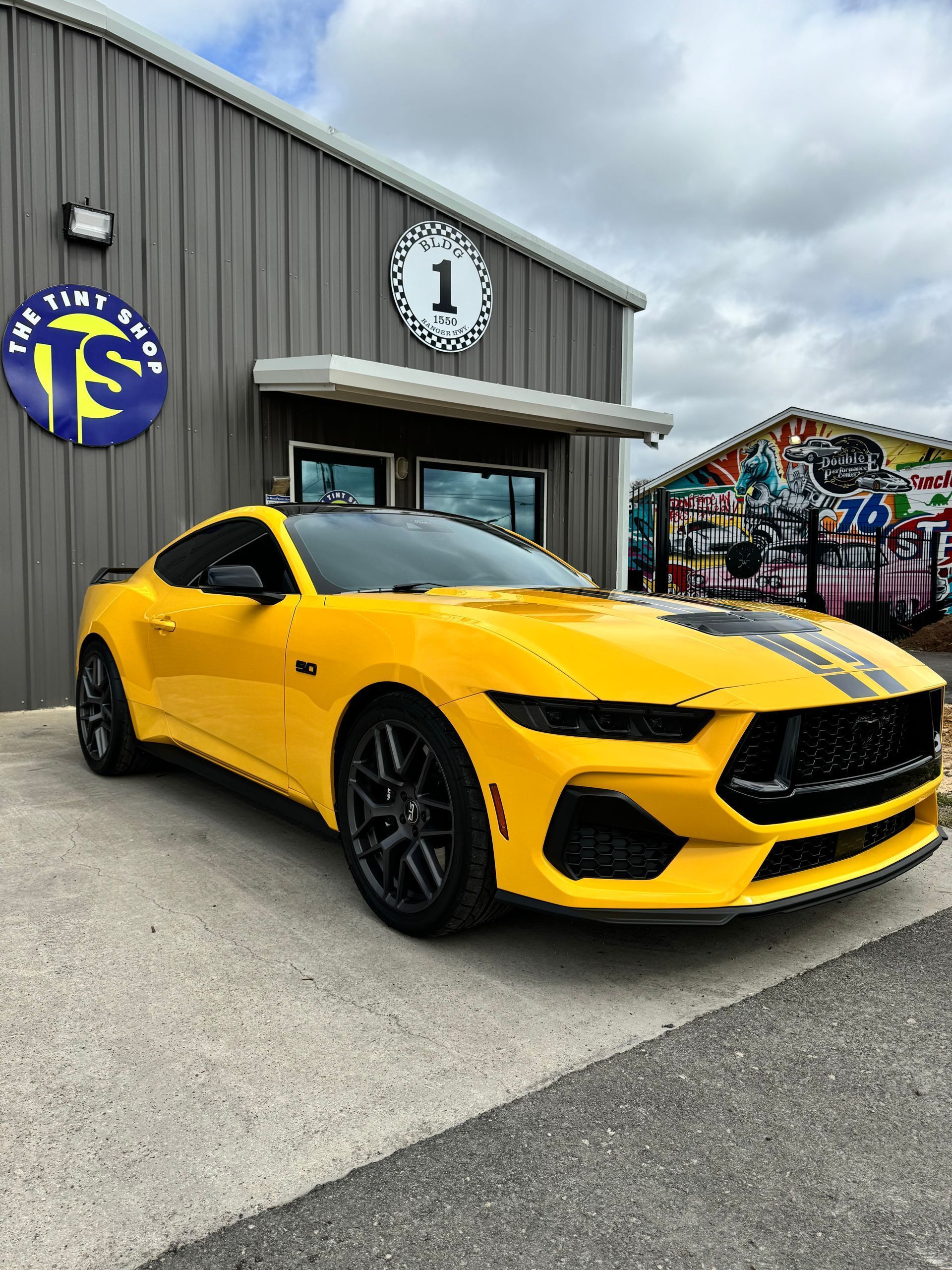 Yellow Ford Mustang in front of a shop with the words 