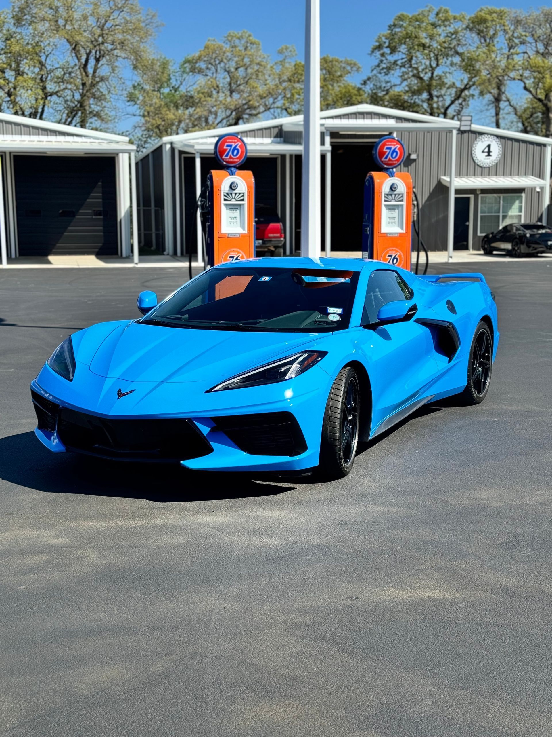 Bright blue sports car parked in front of vintage gas pumps and a garage.