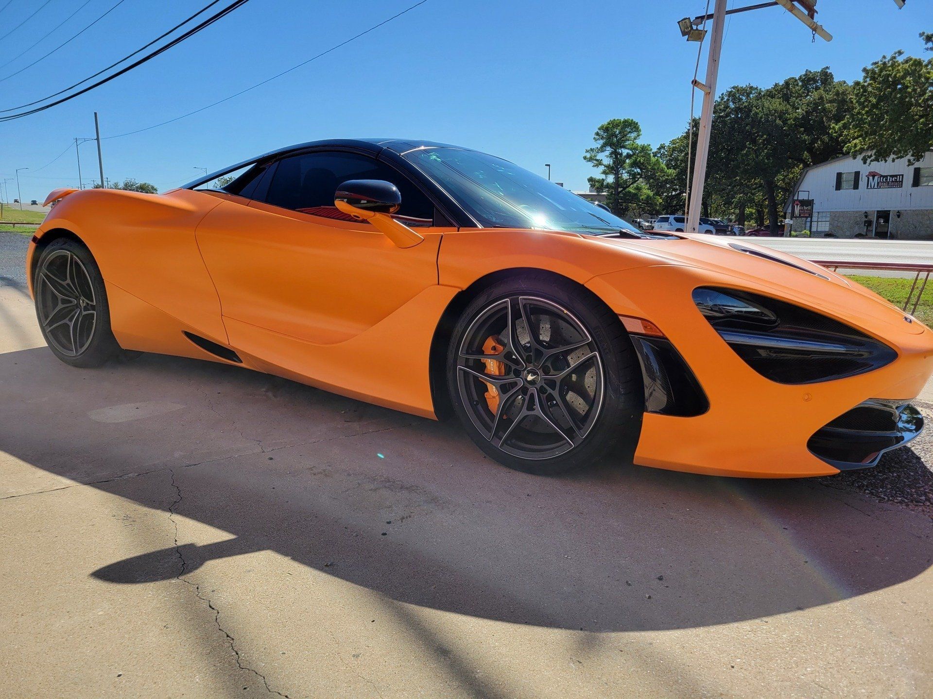 Orange McLaren sports car parked on a roadside on a sunny day.