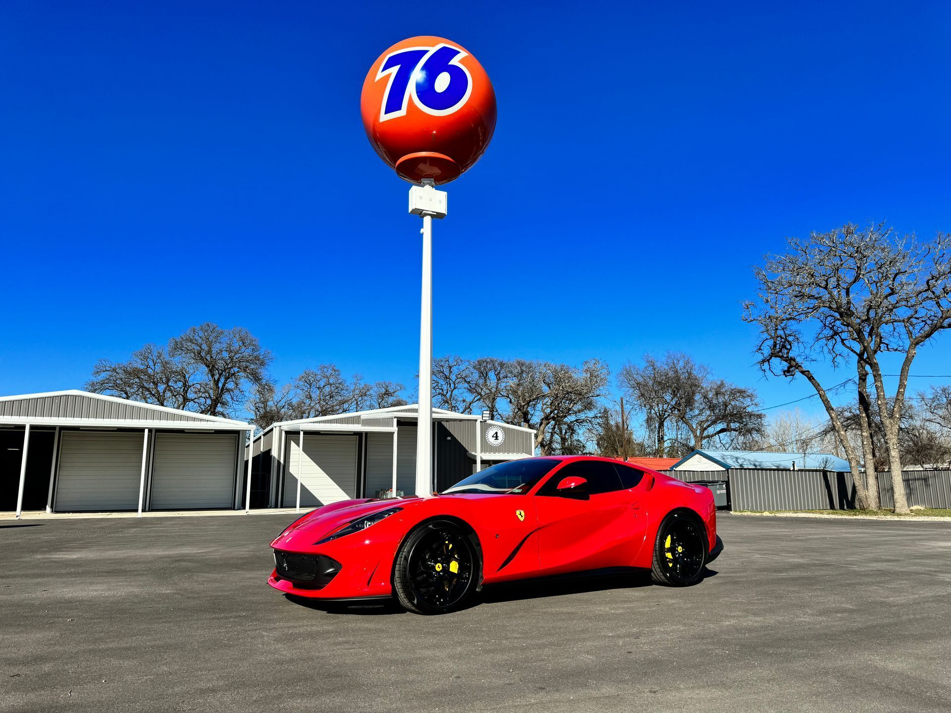 Red Ferrari sports car parked under a 76 gas station sign on a sunny day.