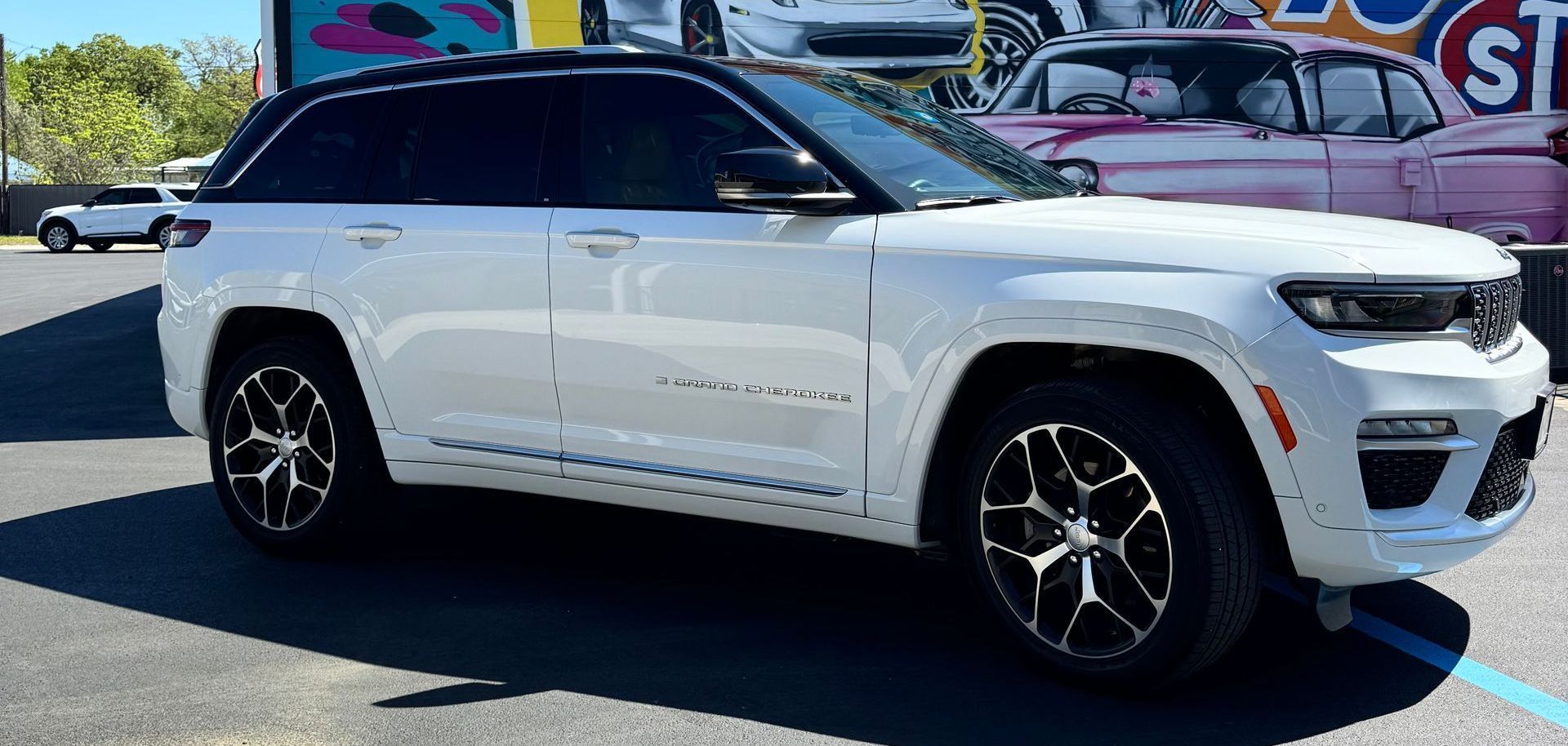 White Jeep Grand Cherokee SUV parked on asphalt. Black roof and wheels.
