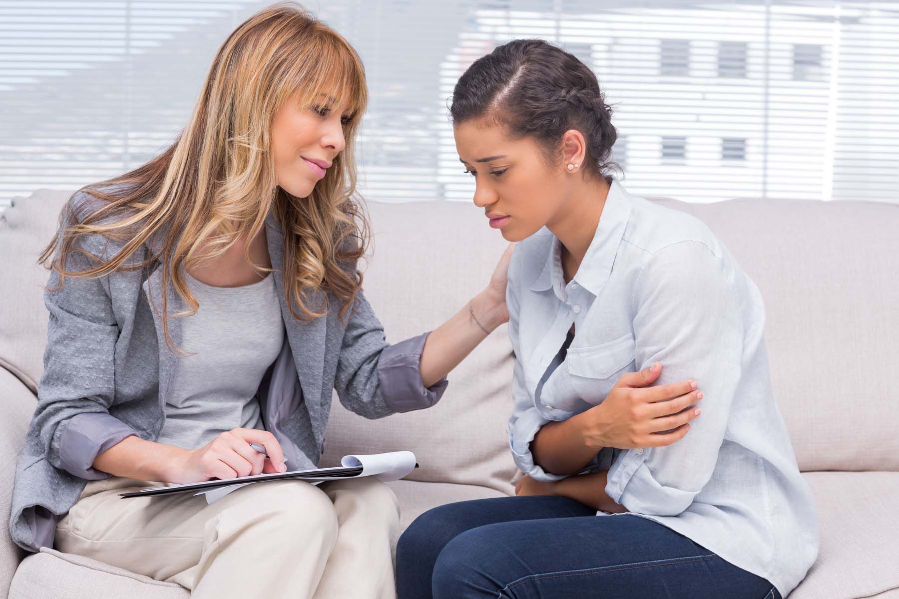 A woman is comforting another woman while sitting on a couch.