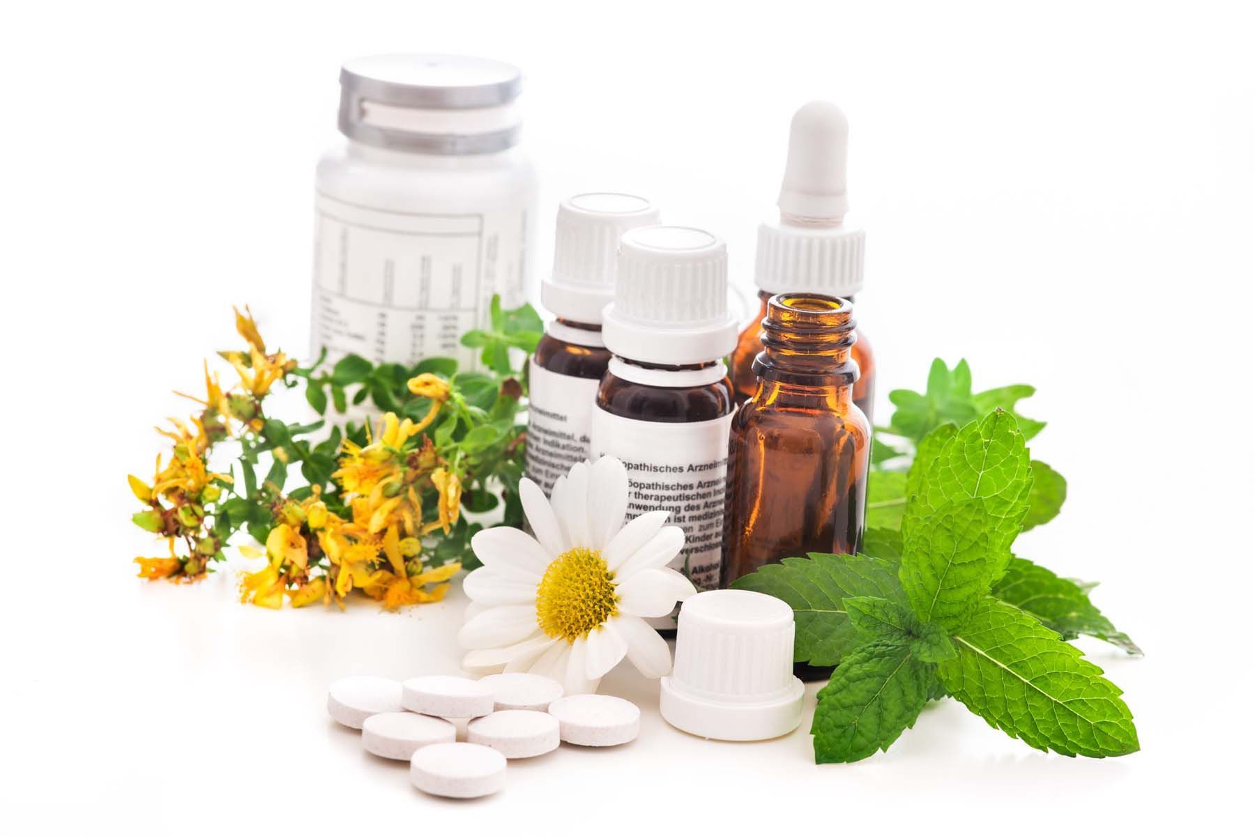 A group of bottles , pills , flowers and mint leaves on a white background.