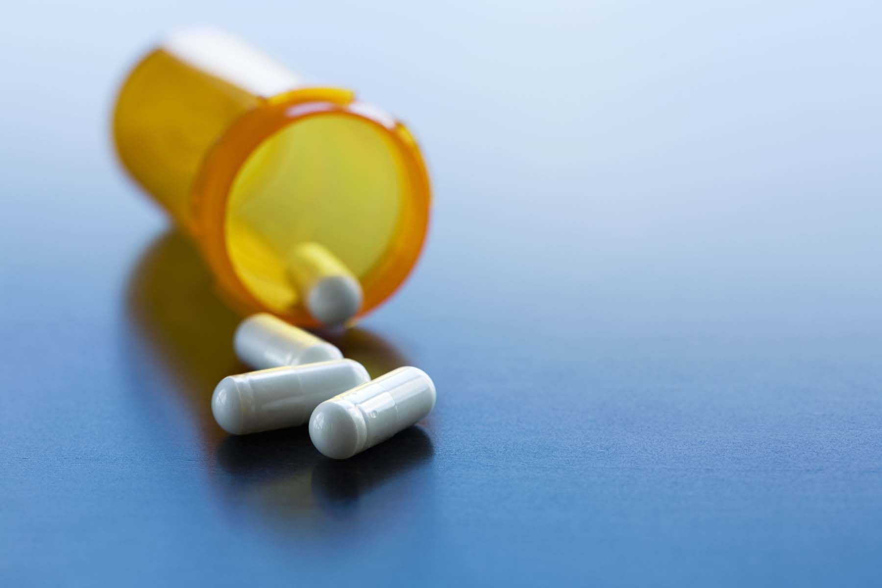 A bottle of pills is spilling out onto a blue surface.