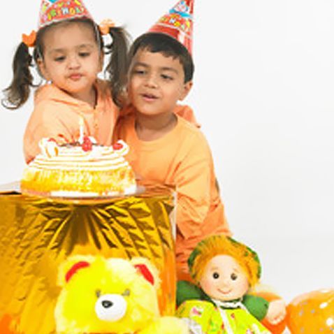 A boy and a girl sitting next to a birthday cake.