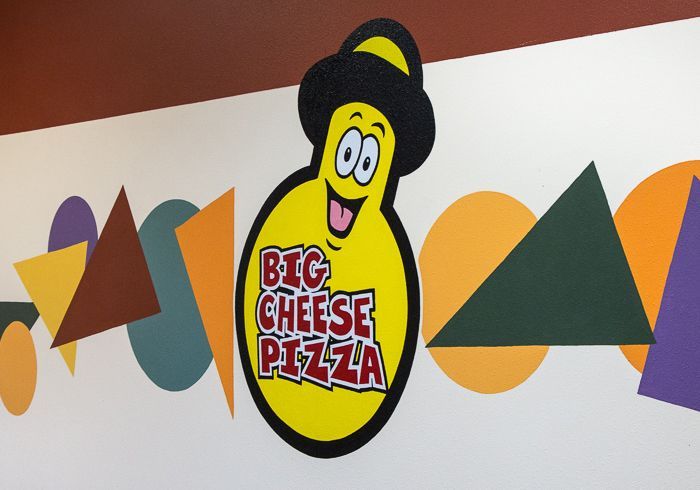 A big cheese pizza logo on a wall