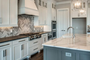 A kitchen with white cabinets , black counter tops , and a large island.