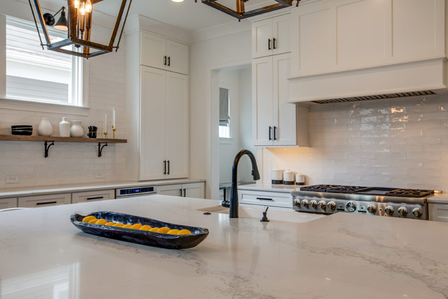 A kitchen with white cabinets , a stove , a sink , and a bowl on the counter.