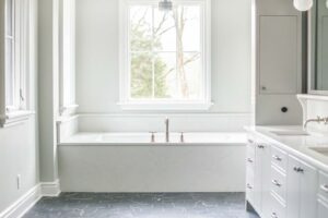 A bathroom with a tub , sink , mirror and window.