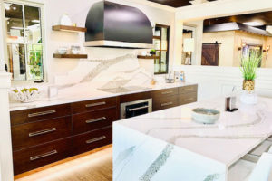 A kitchen with white counter tops , wooden cabinets , stainless steel appliances and a large island.