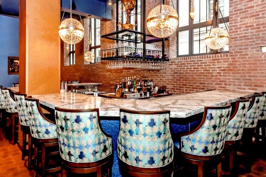 A restaurant with a long bar and chairs and a brick wall.