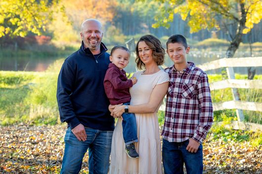 A family is posing for a picture in front of a white fence.