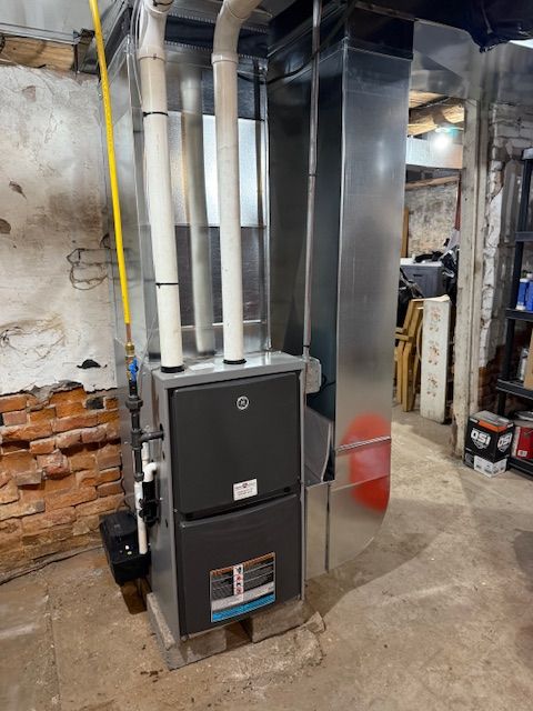 A furnace is sitting in a basement next to a brick wall.