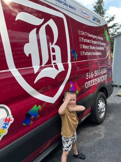 A little boy is standing in front of a red van with the letter b on it