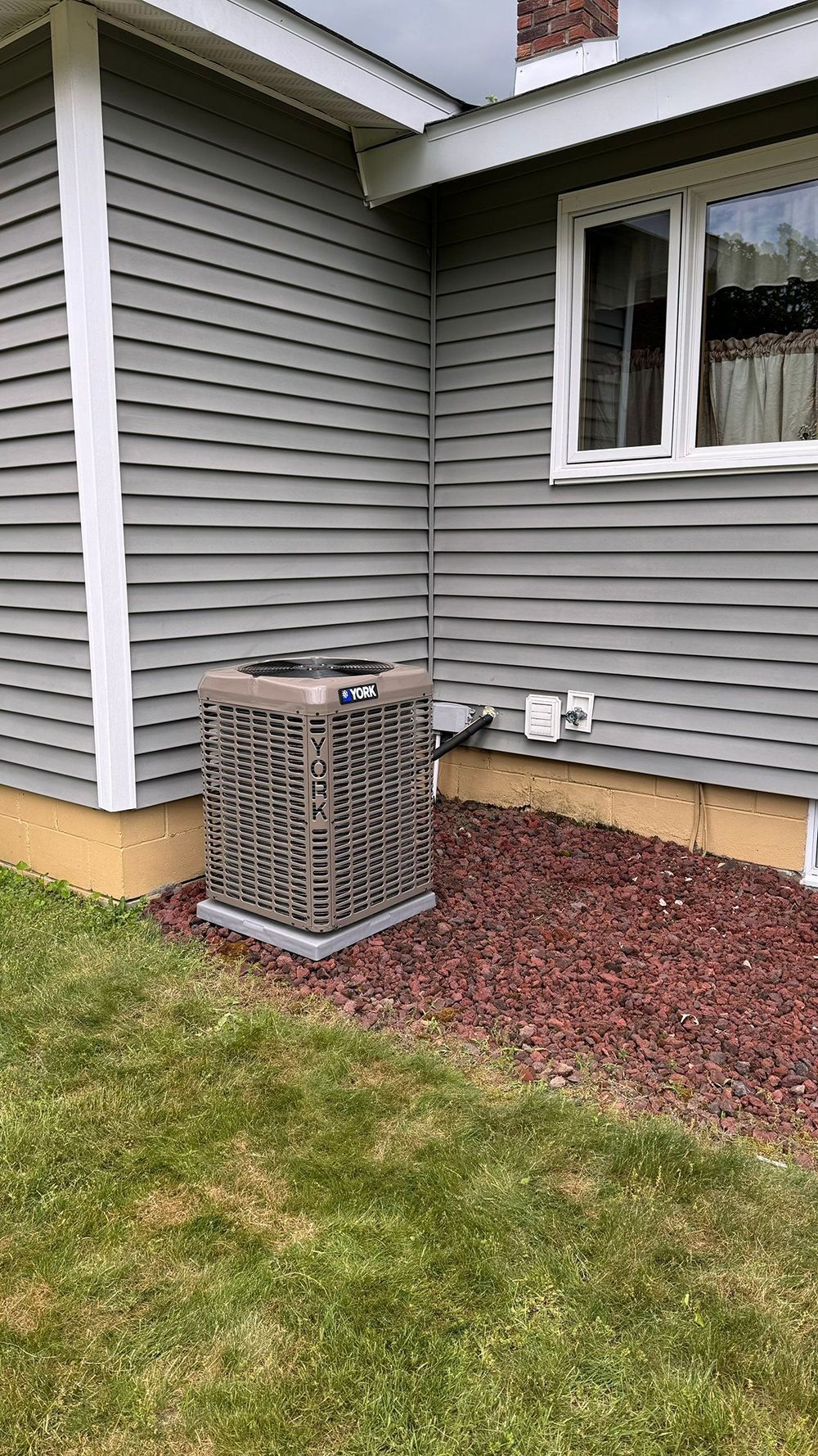 An air conditioner on the side of a house next to a window.