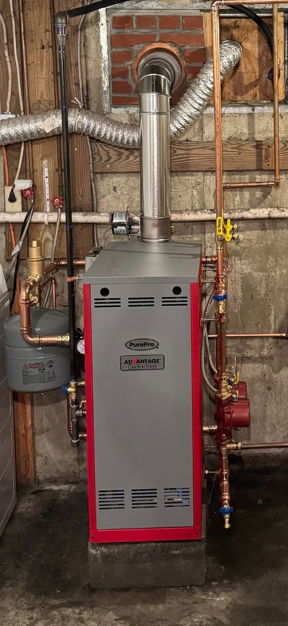 A red and gray boiler is sitting in a basement next to a brick wall.
