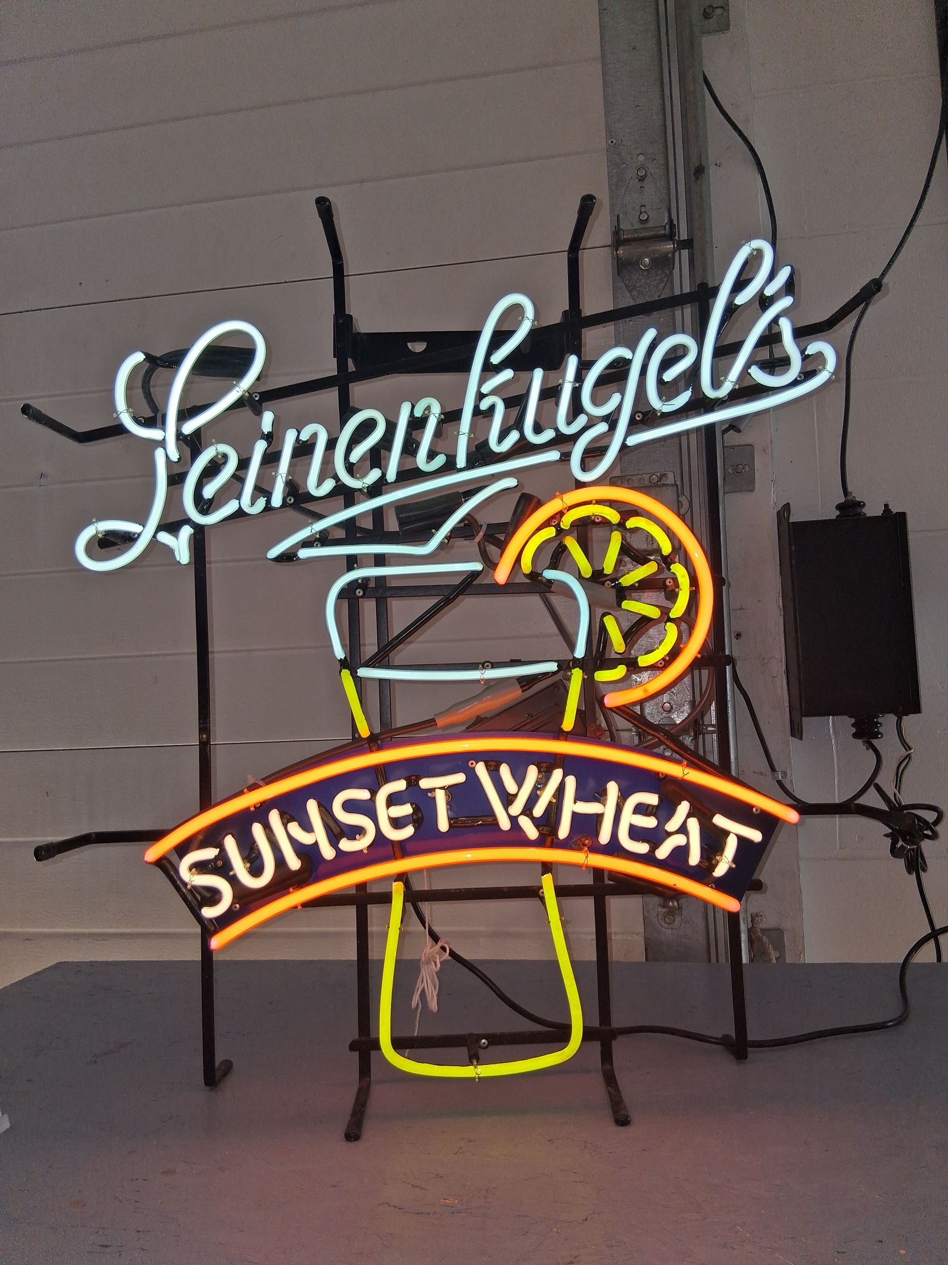 Neon beer sign reading “Leinenkugel’s” and “Sunset Wheat” on a wall.