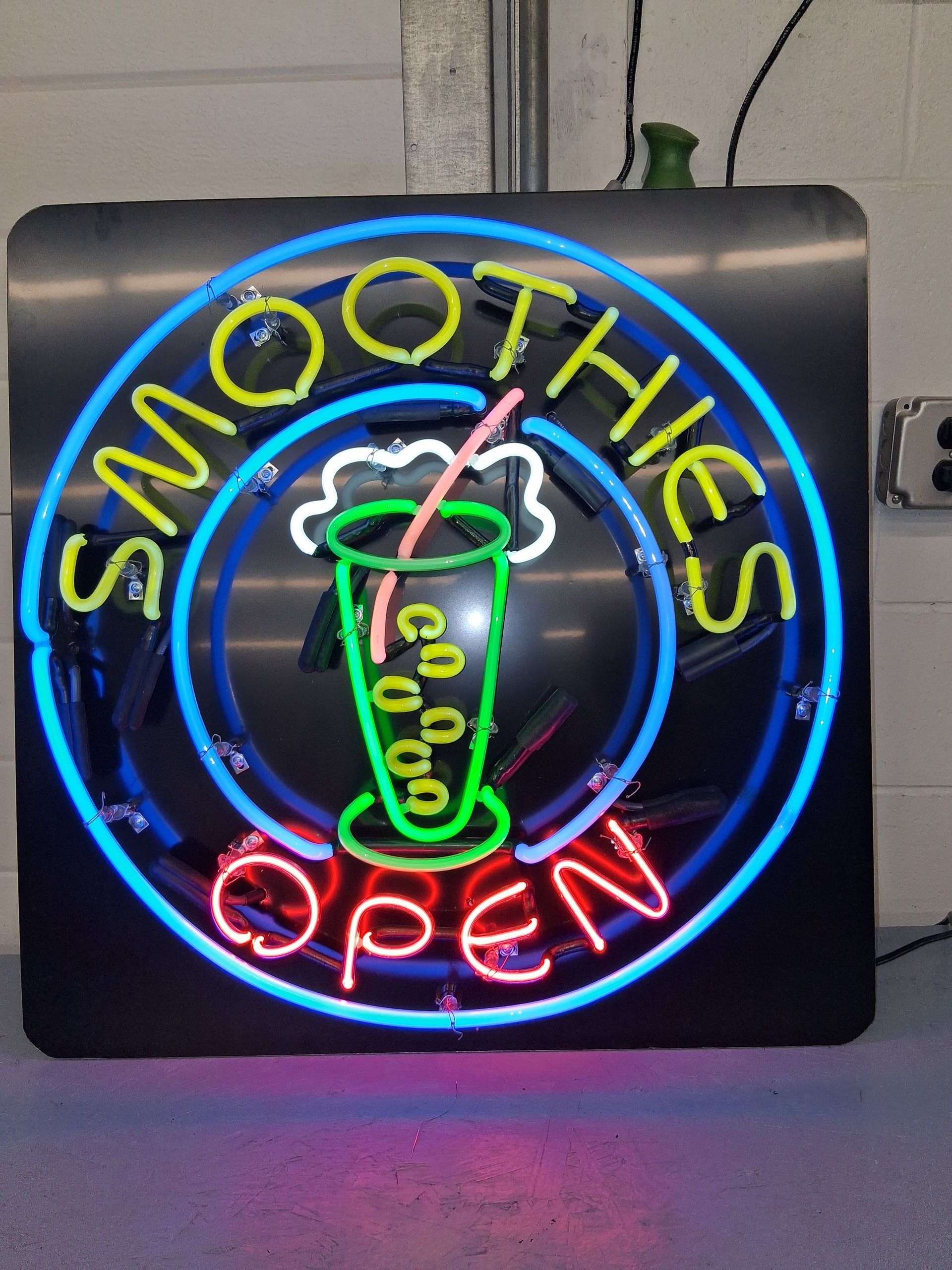 Neon “SMOOTHIES OPEN” sign with a green smoothie cup on a black background.