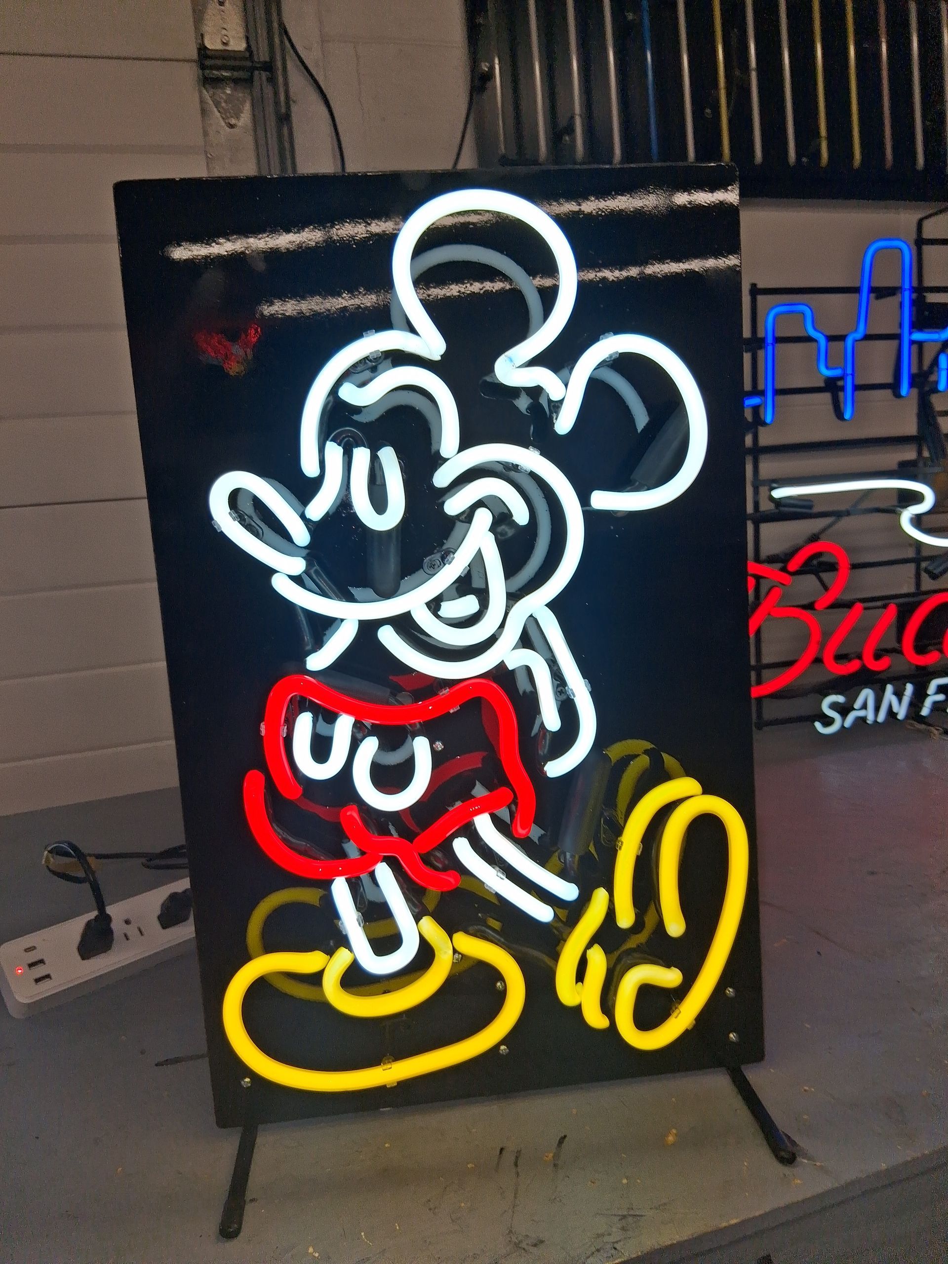 Neon outline of Mickey Mouse on a black signboard, with white, red, and yellow glowing lines.