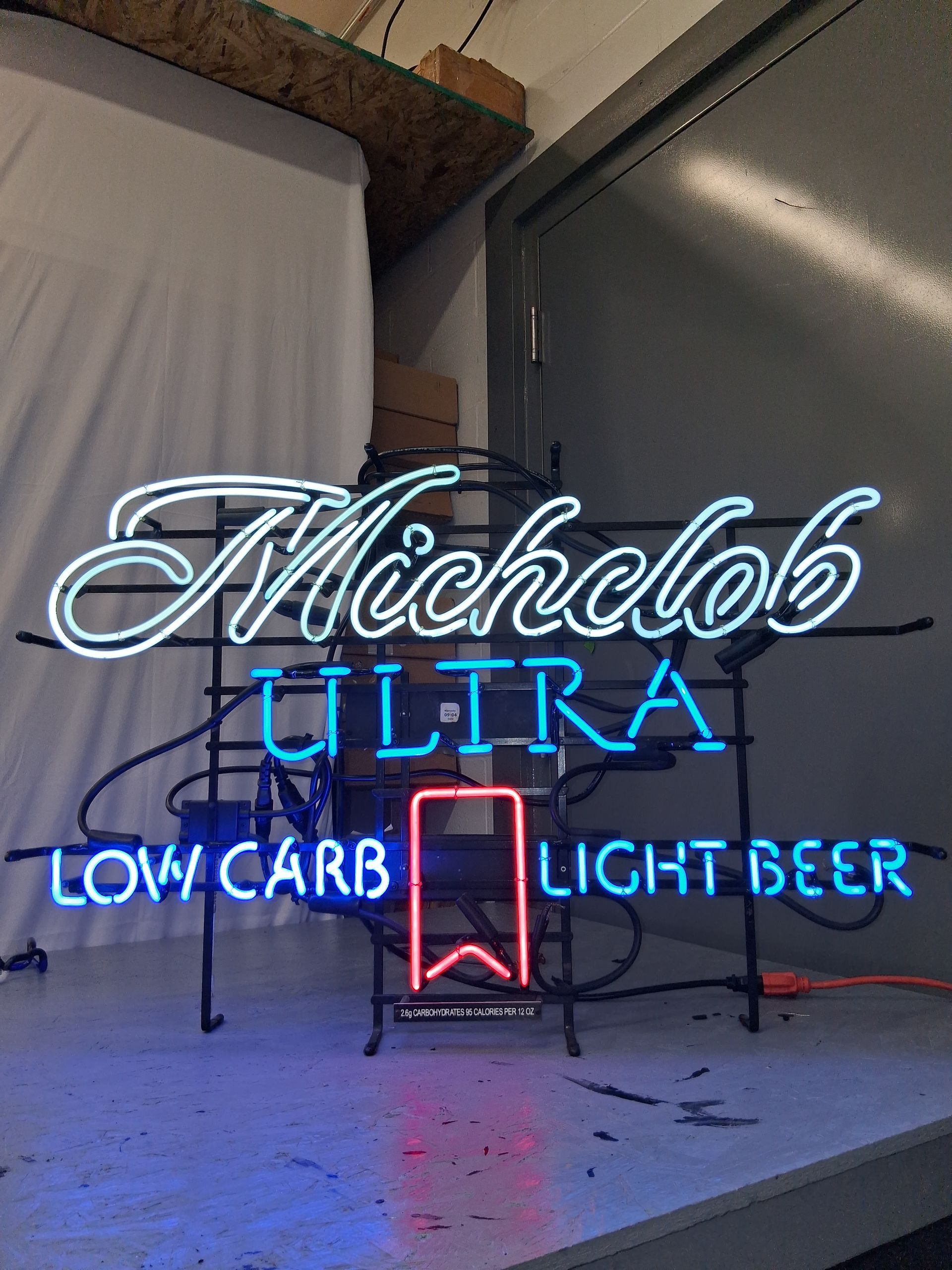 Neon Michelob Ultra sign with blue and white lettering reading “Low Carb Light Beer” indoors
