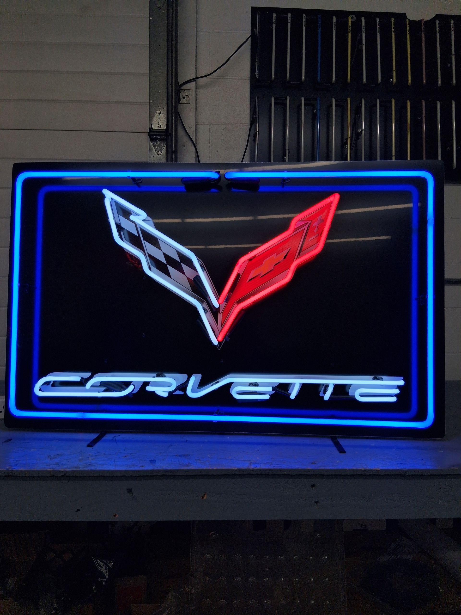 Blue neon Corvette sign with red and white emblem on a dark wall