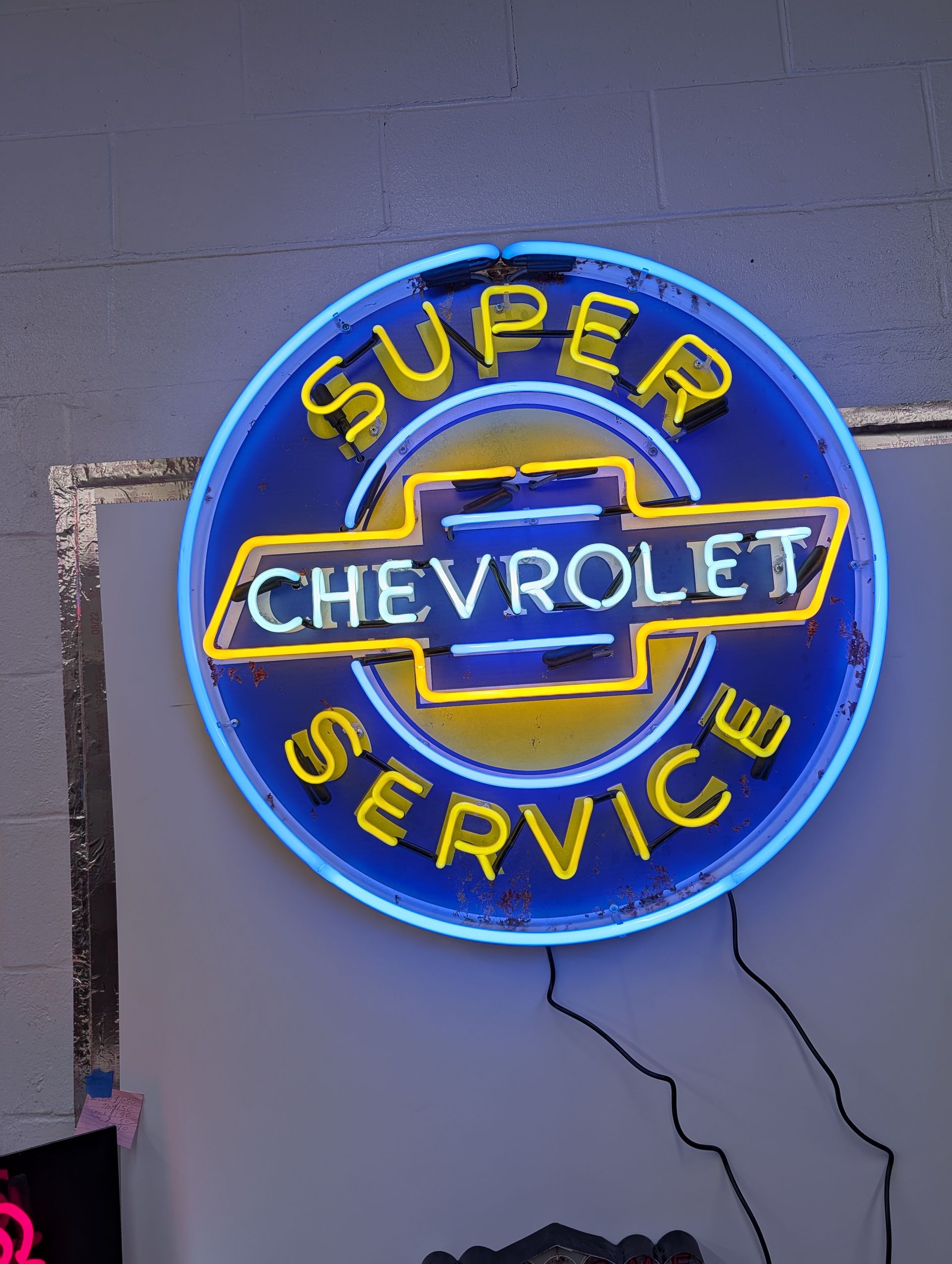 Blue neon Chevrolet Super Service sign on a gray wall with a hanging cord.