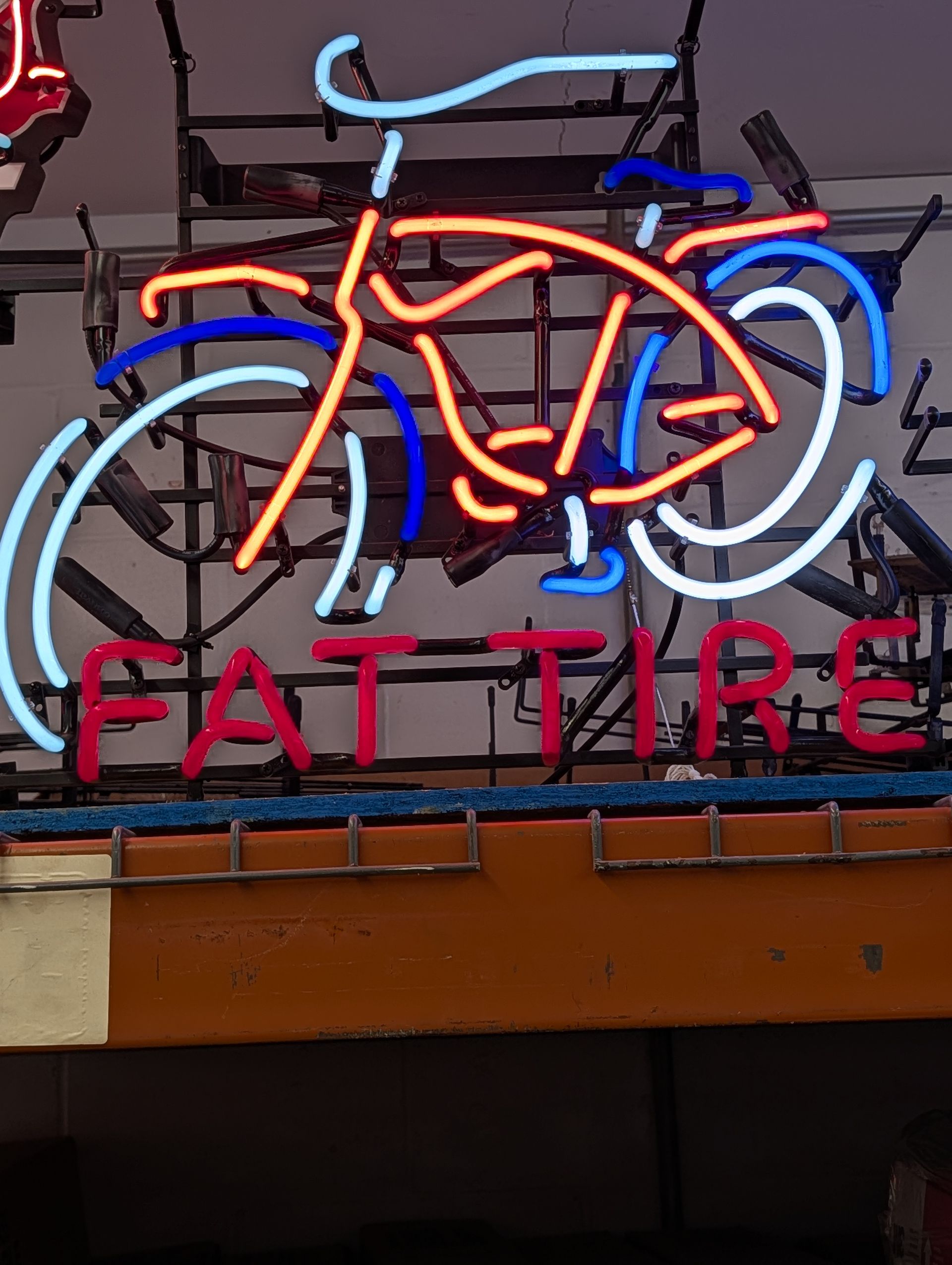 Neon bicycle sign with orange, blue, and white lights above the words “FAT TIRE”