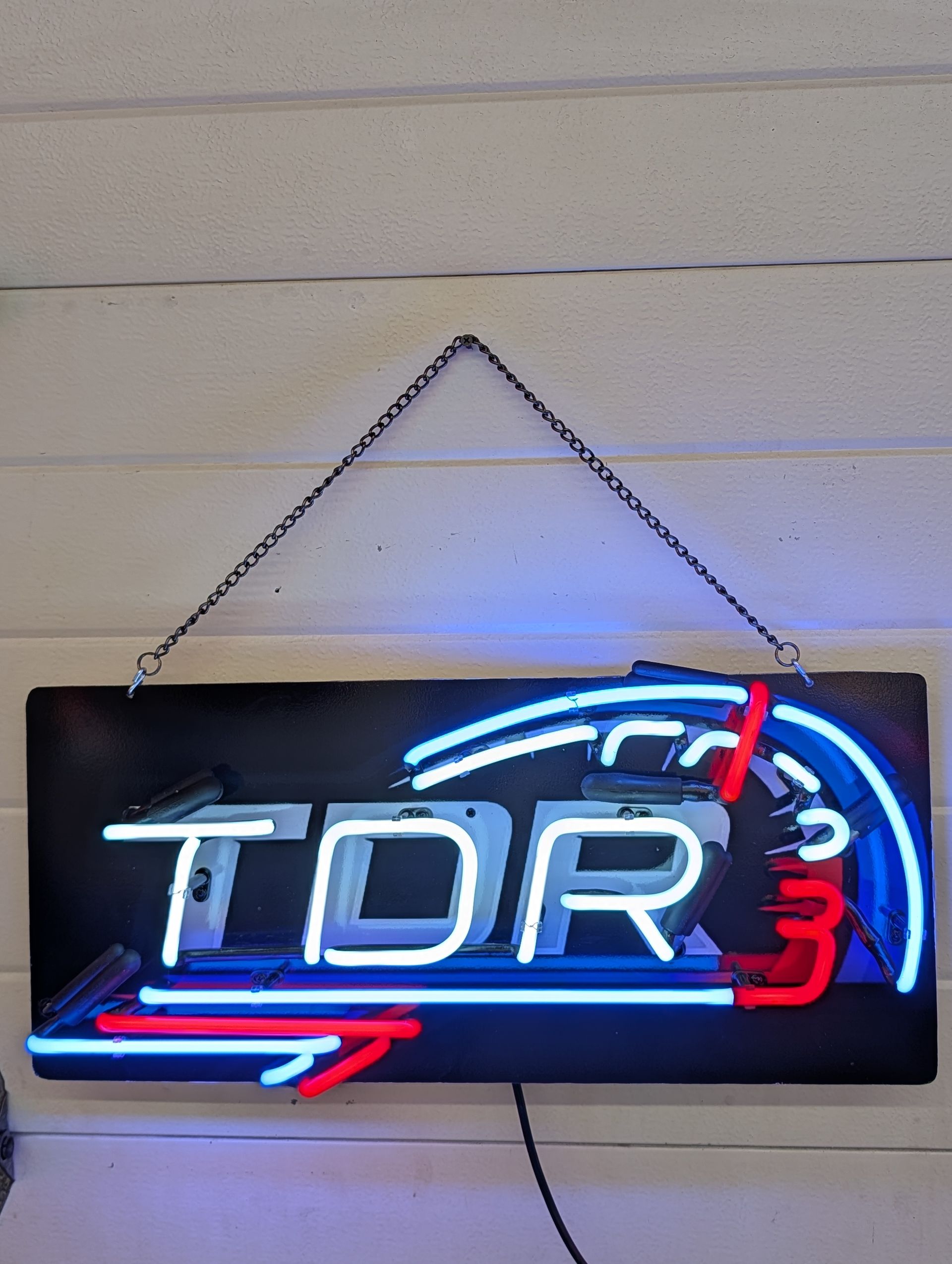 Neon TDR sign in blue, white, and red hanging on a wall by a chain
