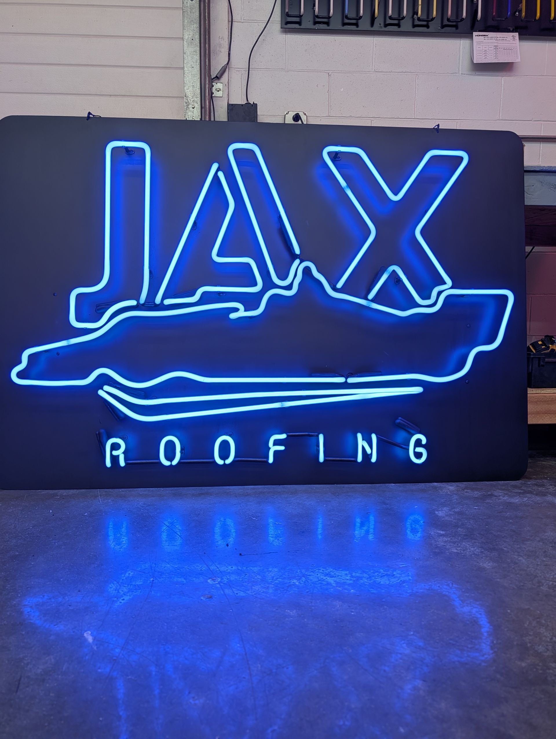 Blue neon JAX Roofing sign with reflected glow on a glossy floor