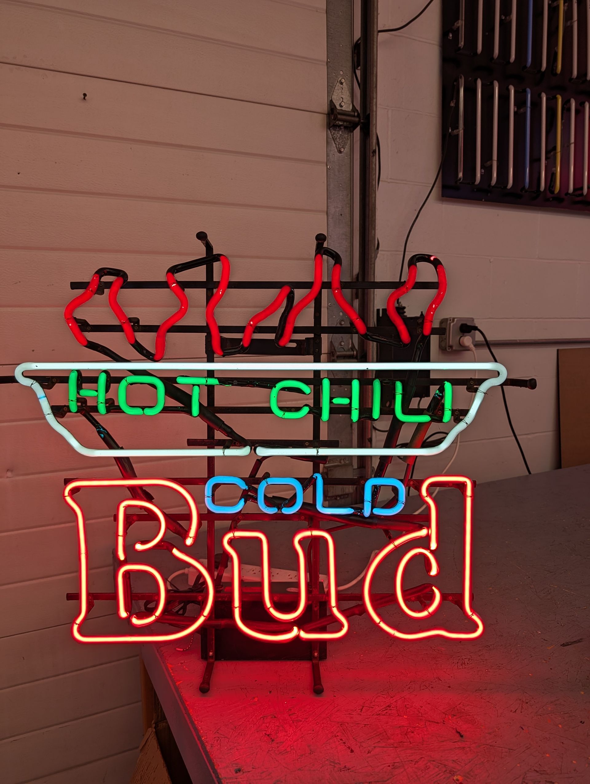 Neon “HOT CHILI” and “COLD Bud” sign glowing red, green, and blue on a wall.