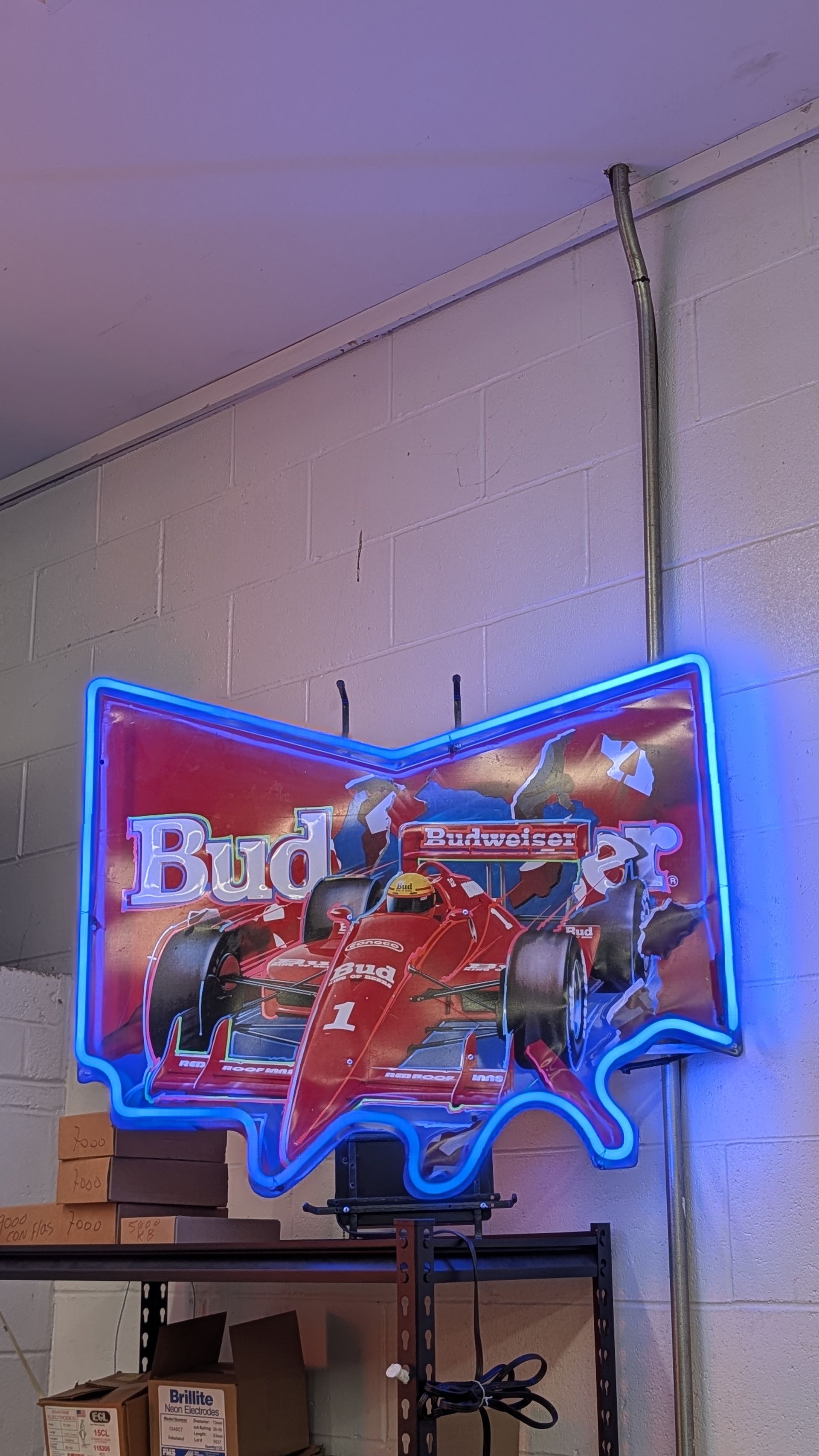 Blue neon Budweiser racing sign on a wall above a workbench in a room.