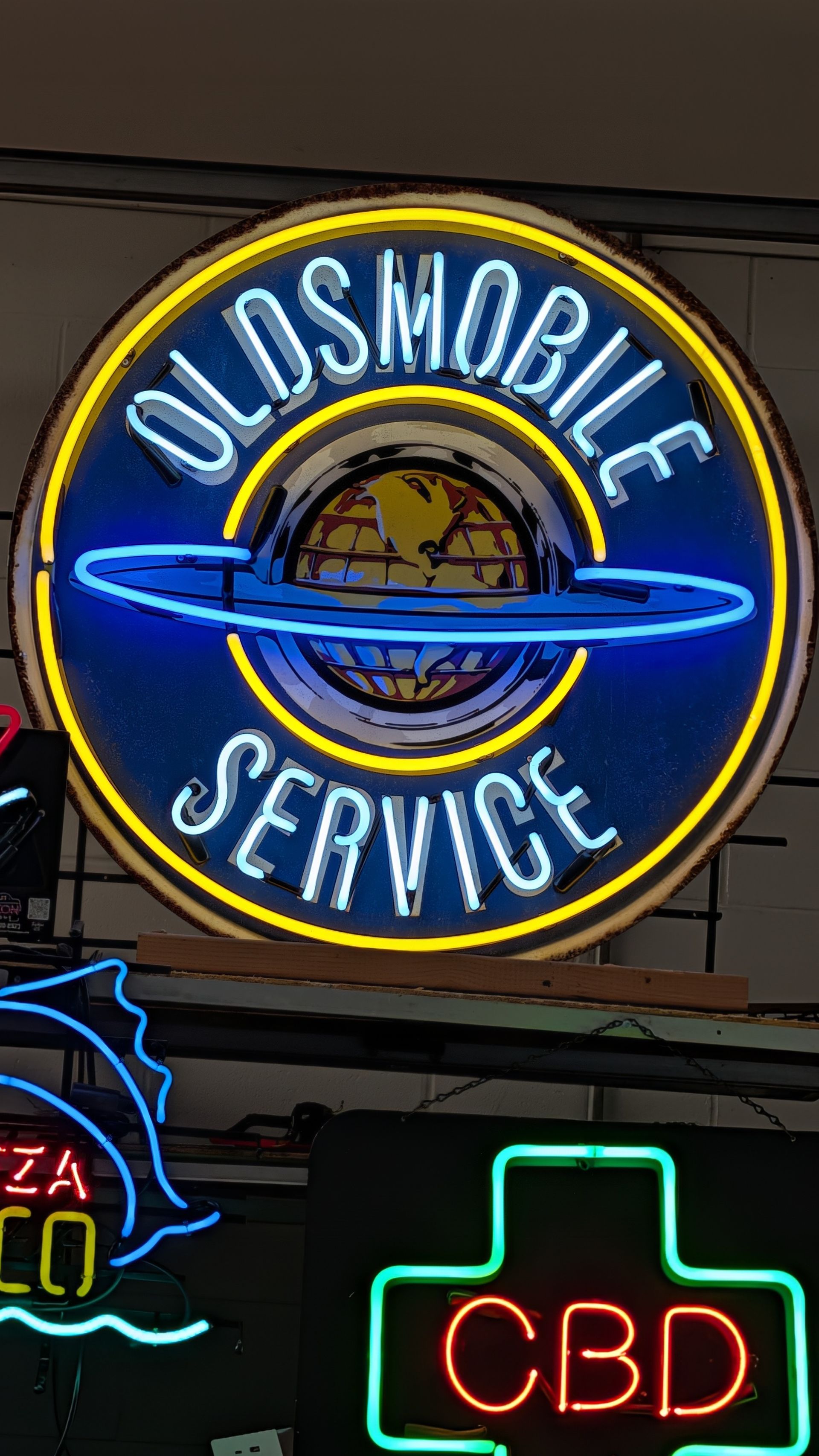 Neon Oldsmobile Service sign with blue car logo above a glowing CBD sign.