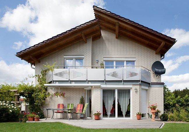 Two-story white house with balcony, patio furniture, and a green lawn under a partly cloudy sky