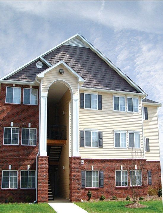 Three-story apartment building with tan siding, red brick, and a central arched stairwell entrance.