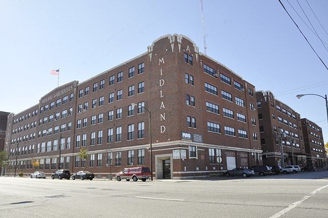 Large brick hospital building on a city street corner, with an American flag and parked cars outside.